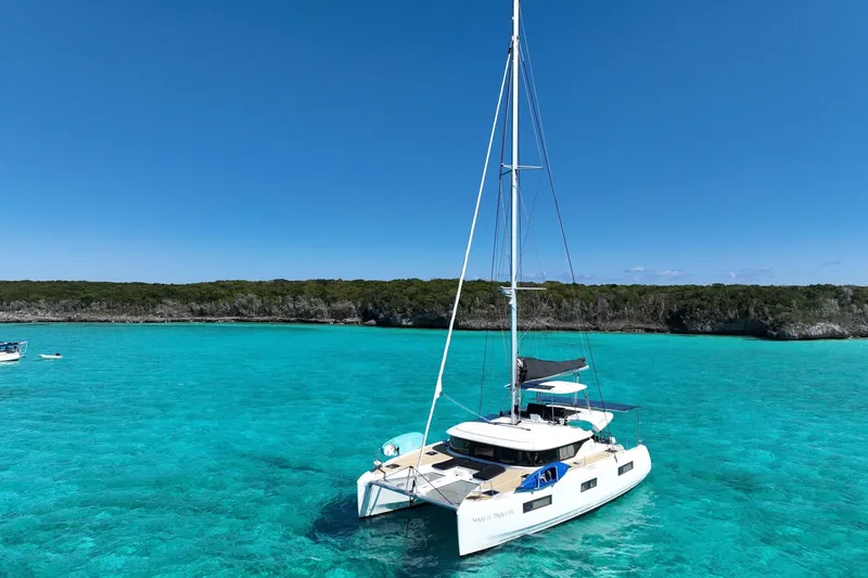 Slide: The Image of 2021 Lagoon 46 catamaran sailing in clear turquoise waters near a lush coastline. - 2
