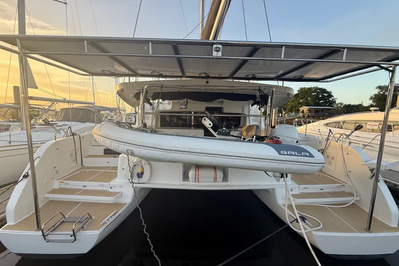 Slide: The Image of 2021 Lagoon 46 catamaran with dinghy, docked at sunset, showcasing spacious deck and modern design. - 7