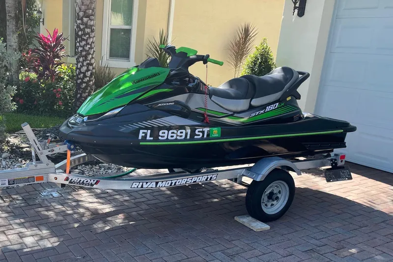 The Image of A green 2020 Kawasaki Jetski STX 160LX sits on a trailer in front of a house. - 0