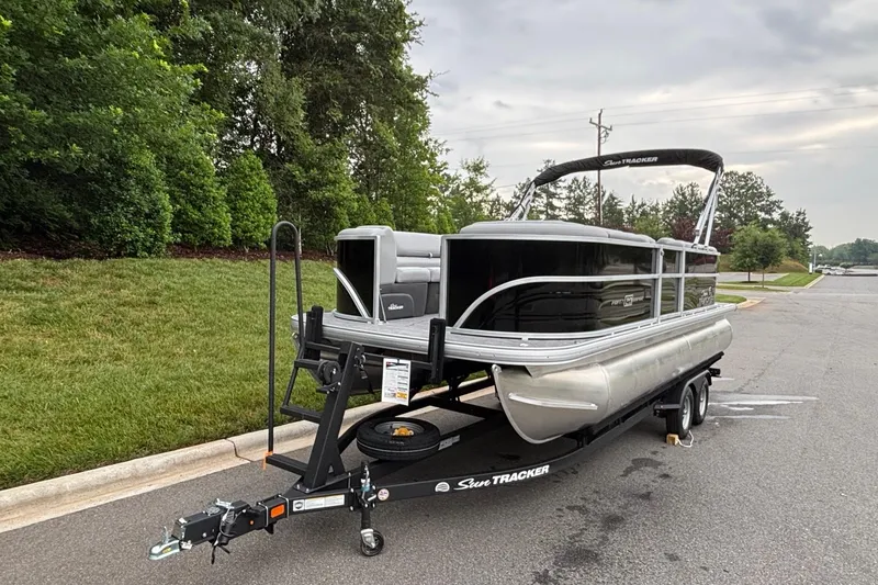 Slide: The Image of 2026 Sun Tracker Party Barge 20 DLX pontoon boat on trailer, parked near greenery. - 2