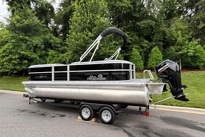 Slide: The Image of 2026 Sun Tracker Party Barge 20 DLX pontoon boat on trailer, parked near lush greenery. - 3