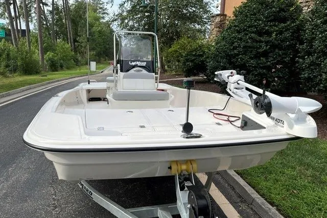 Slide: The Image of 2026 Mako Pro Skiff 15 CC boat on trailer, parked on a road near greenery. - 2