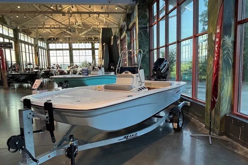 Slide: The Image of 2026 Mako Pro Skiff 13 CC boat displayed in a showroom on a trailer. - 2
