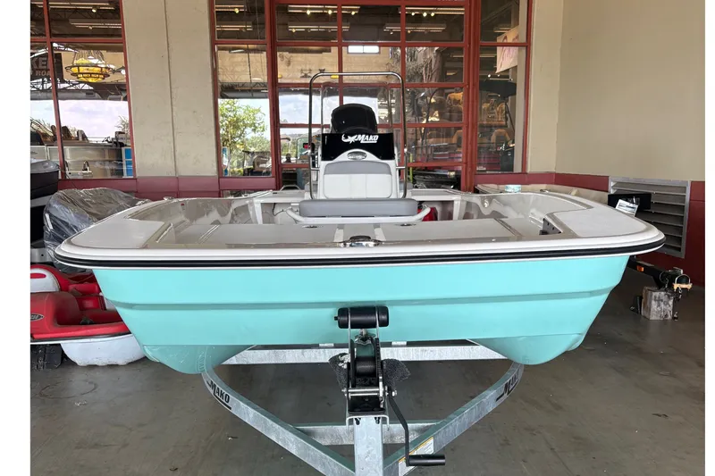 Slide: The Image of A turquoise 2026 Mako Pro Skiff 17 CC sits on a trailer in a warehouse. - 1