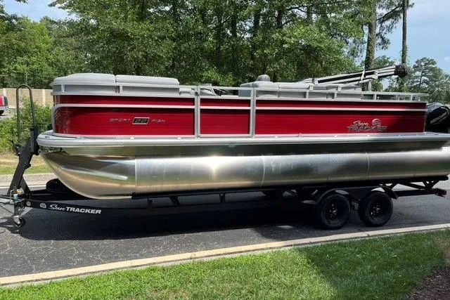 Slide: The Image of 2026 Sun Tracker SportFish 22 XP3 pontoon boat with red and silver design on a trailer. - 1