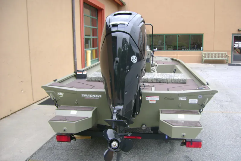 Slide: The Image of 2026 Tracker Grizzly 1860 CC boat with powerful outboard motor, parked outside a building. - 7