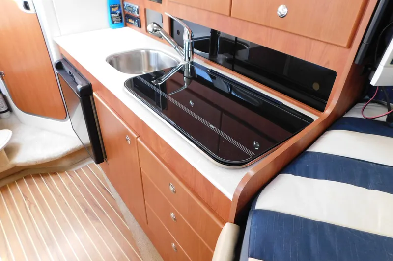 Slide: The Image of 2009 Bayliner 300 yacht kitchen with sink, stove, and wooden cabinetry. - 57