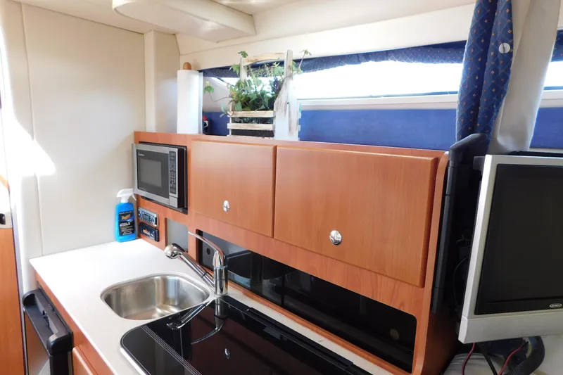 Slide: The Image of 2009 Bayliner 300 yacht kitchen with sink, microwave, and wooden cabinets. - 58