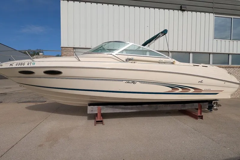 Slide: The Image of 1998 Sea Ray 260 Signature boat on display, beige hull with blue accents, parked outdoors. - 0