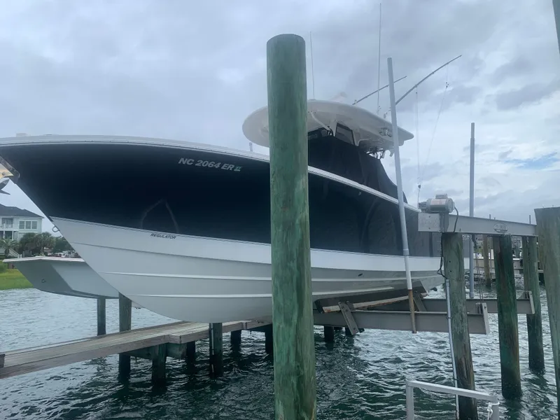 Slide: The Image of A 2020 Regulator 31 boat is on a lift above the water. It features a dark hull. - 3