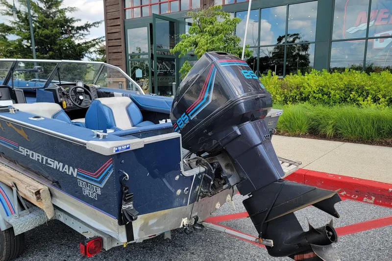 Slide: The Image of 1988 BLUE FINN SPORTSMAN 1700 boat with outboard motor, parked near a modern building. - 3