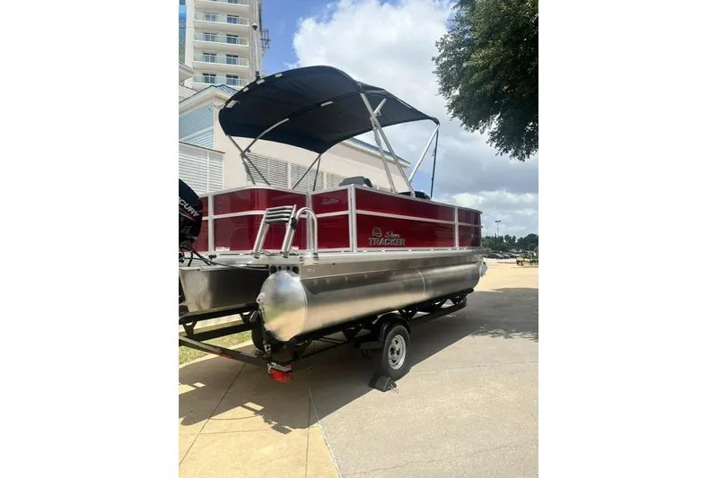 Slide: The Image of 2026 SUNTRACKER pb18 pontoon boat with canopy on trailer, parked near building. - 4