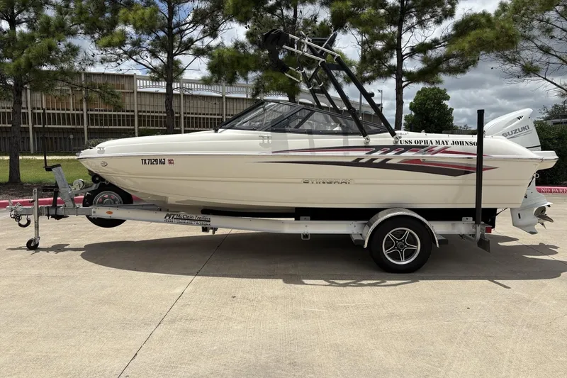 Slide: The Image of 2021 Stingray 204 LR boat on trailer, parked outdoors with trees in background. - 6