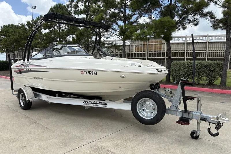 Slide: The Image of 2021 Stingray 204 LR boat on trailer, parked outdoors with trees in background. - 2