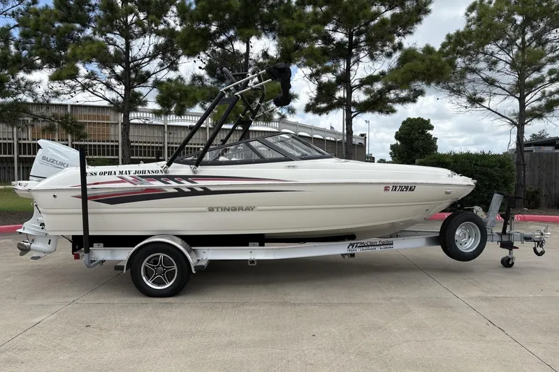 The Image of 2021 Stingray 204 LR boat on trailer, parked outdoors with trees in background. - 1