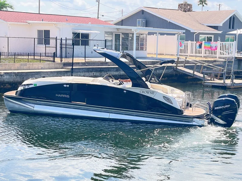 Slide: The Image of A sleek pontoon boat with a black hull and Mercury outboard motor, docked in a calm canal. - 10