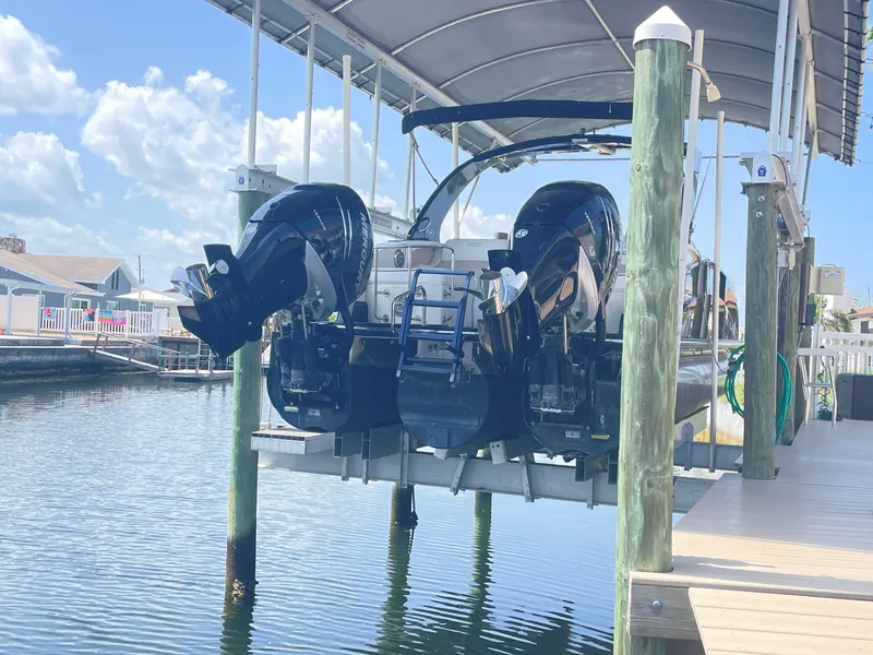 Slide: The Image of A 2015 Harris FloteBote Crown DL 250 is on a boat lift above the water. It features twin outboard engines. - 4