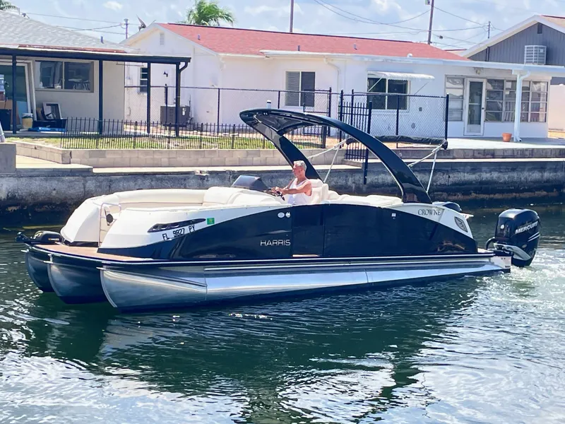 Slide: The Image of A 2015 Harris FloteBote Crown DL 250 cruising on calm waters. It features a sleek design with a black Bimini top. - 11