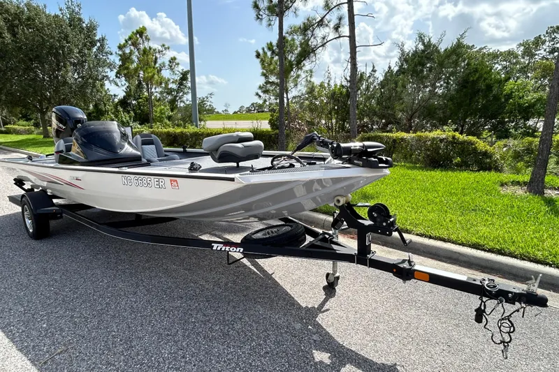 Slide: The Image of 2020 Triton 18 TX boat on trailer, parked on a sunny roadside with lush greenery. - 1