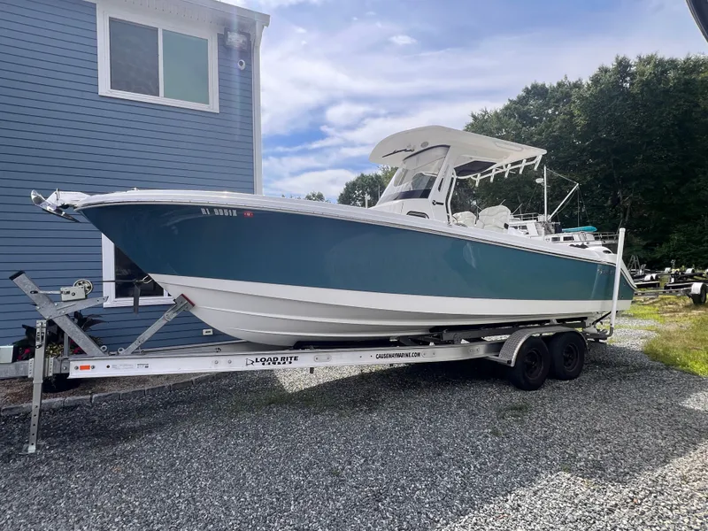Slide: The Image of A 2021 Edgewater 262CC boat on a trailer next to a blue building. - 0