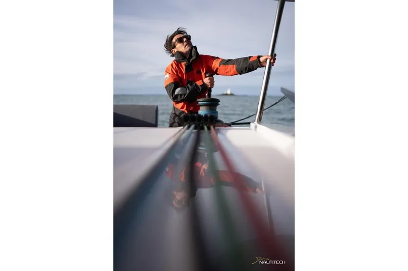 Slide: The Image of A sailor in a red jacket operates a winch on a Nautitech 48 Open catamaran. - 23