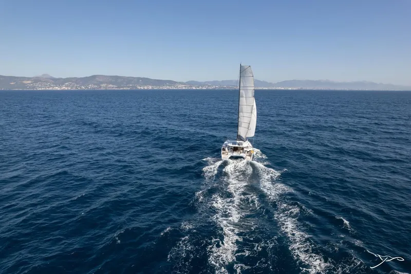 Slide: The Image of A Nautitech 44 Open catamaran sails on open sea with mountains in the background. - 1