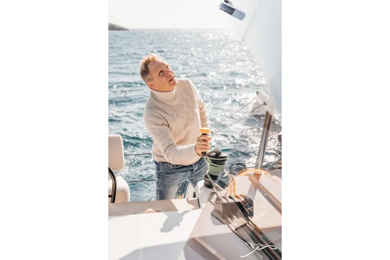 Slide: The Image of A man in a cream sweater operates a winch on a sailboat. - 16