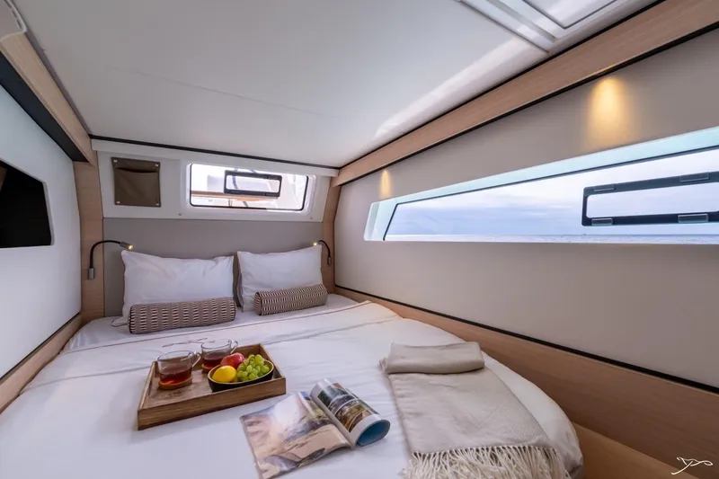 Slide: The Image of Cozy cabin with a double bed, windows, and reading lights. A tray with tea and fruit on the bed. - 48
