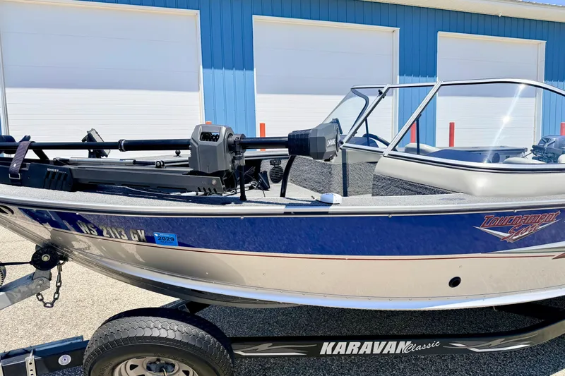 Slide: The Image of 2005 Alumacraft Tournament Sport 175 boat on Karavan trailer, parked near blue building. - 6