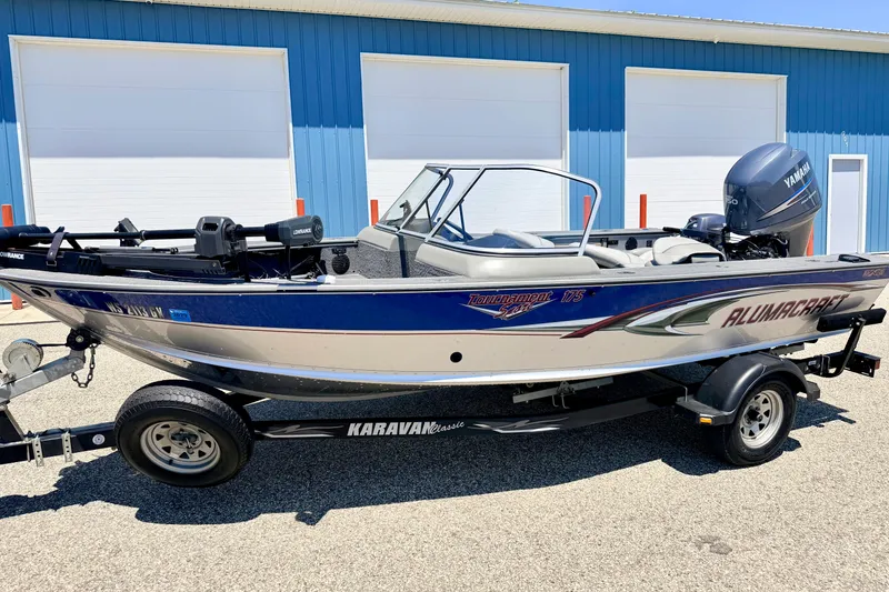 Slide: The Image of 2005 Alumacraft Tournament Sport 175 boat on trailer, parked near blue building. - 5