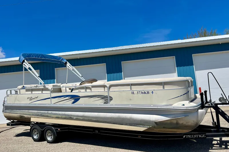 The Image of 2004 Bennington 2875RLX pontoon boat on trailer, parked outside blue building. - 0