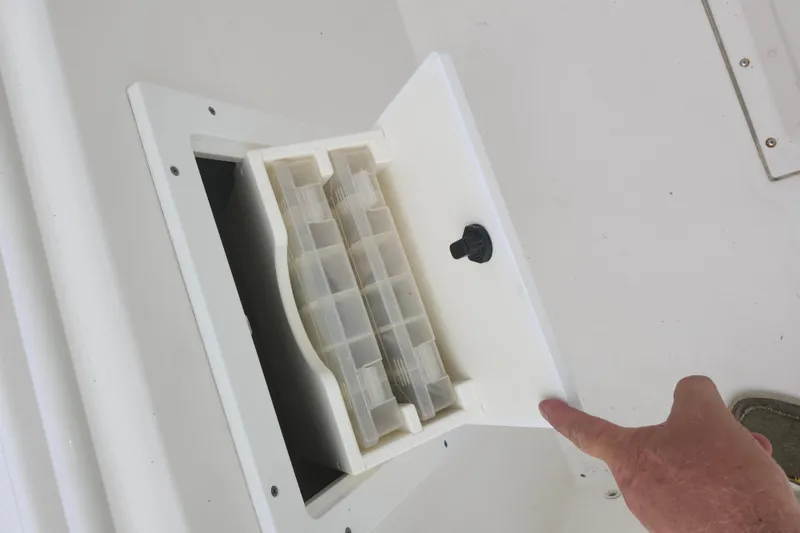 Slide: The Image of Storage compartment on a 2007 Edgewater 228CC boat, featuring a tackle box and latch. - 24