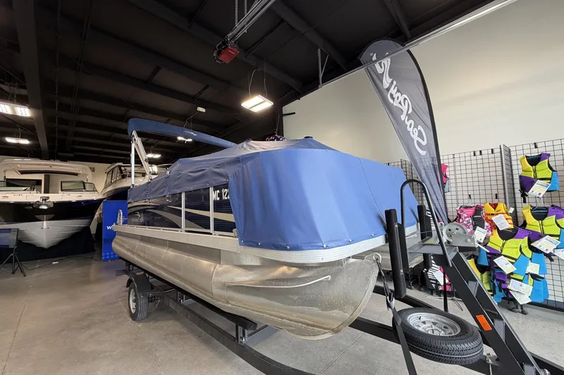 Slide: The Image of 2010 Bennington 20SFi pontoon boat in showroom, covered with blue tarp, surrounded by life jackets. - 1