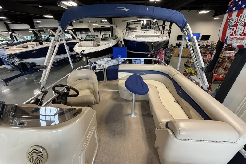Slide: The Image of 2010 Bennington 20SFi pontoon boat interior with beige seating and blue accents in showroom. - 13