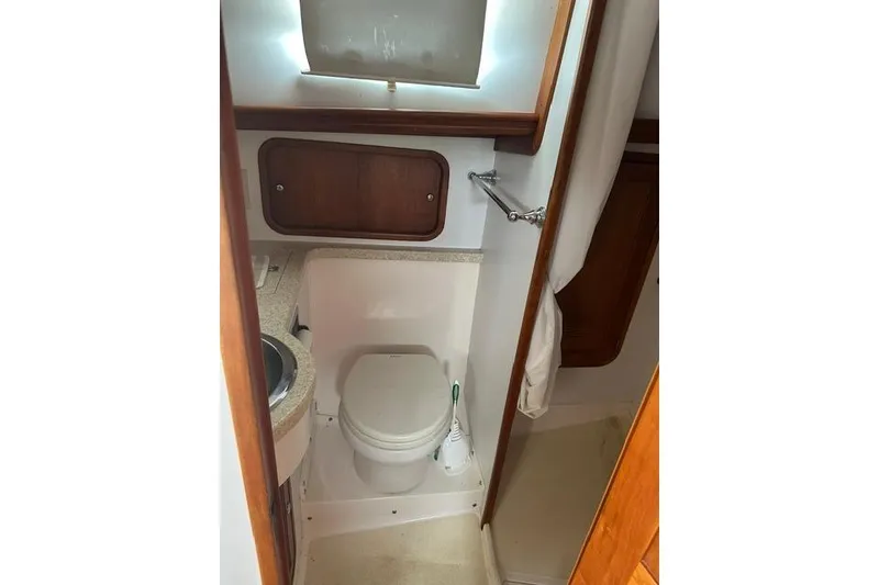 Slide: The Image of Compact bathroom in a 2002 Legacy Express boat, featuring a toilet and wooden cabinetry. - 23