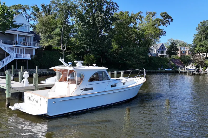 Slide: The Image of A 2002 Legacy Express boat docked by waterfront homes, surrounded by lush trees. - 2