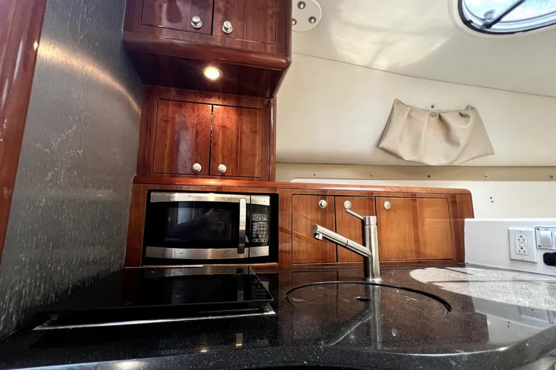 Slide: The Image of 2004 Century 3200 Walk-Around boat kitchen with microwave, sink, and wooden cabinets. - 67