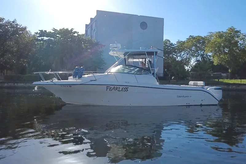 Slide: The Image of 2004 Century 3200 Walk-Around boat named "Fearless" on calm water near trees and building. - 2