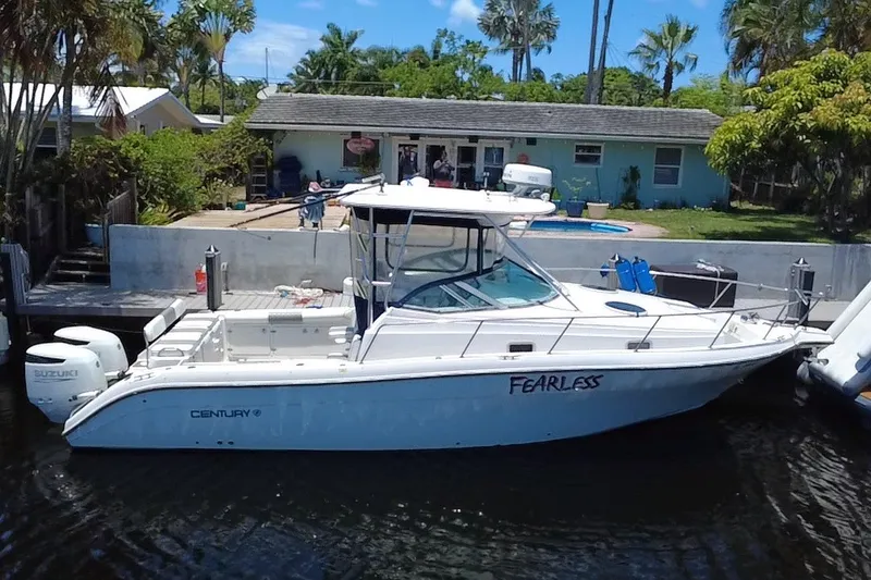 Slide: The Image of 2004 Century 3200 Walk-Around boat named "Fearless" docked near a house with palm trees. - 2