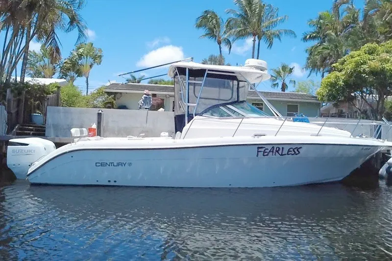 Slide: The Image of 2004 Century 3200 Walk-Around boat named "Fearless" docked near tropical trees. - 3