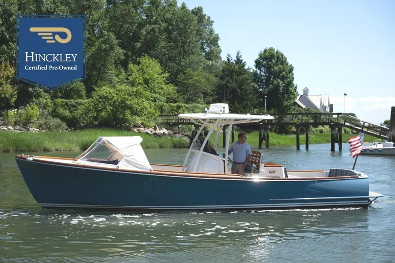 The Image of 2021 Hinckley Talaria 29C on calm water with American flag and lush landscape. - 0