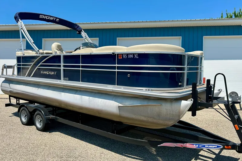Slide: The Image of 2017 Starcraft CX 23 RE pontoon boat on trailer, parked outside a blue building. - 2