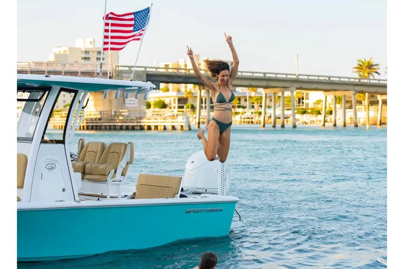Slide: The Image of Manufacturer Provided Image: Woman jumping off 2025 Sportsman Masters 227 Bay Boat, American flag waving, sunny day. - 2