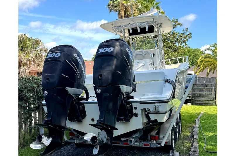 Slide: The Image of 2014 Mako 284 Center Console boat with dual Mercury 300 engines, parked outdoors. - 2