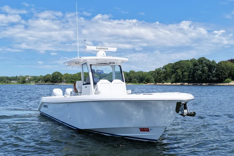 Slide: The Image of 2027 Everglades 315 Center Console boat on water, clear sky, lush shoreline. - 2