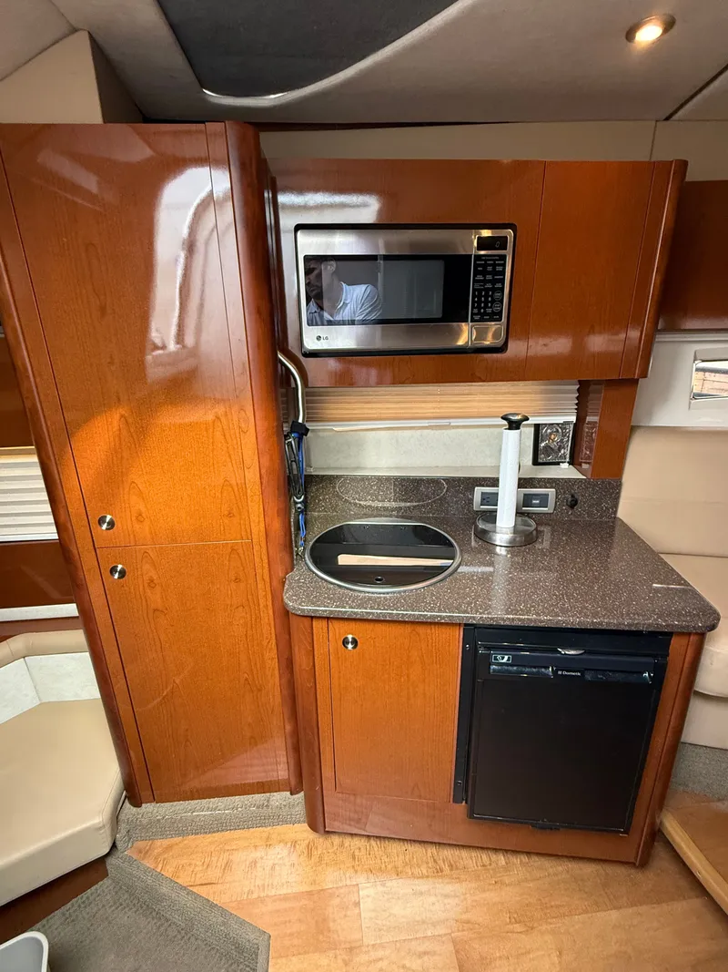 Slide: The Image of The 2013 Sea Ray 370 Venture's galley features wooden cabinets, a microwave, and a sink. - 33