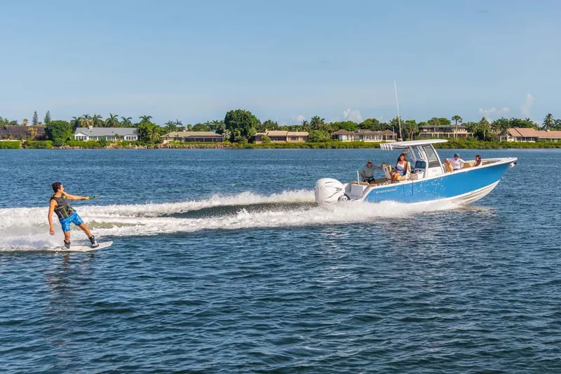 Slide: The Image of Manufacturer Provided Image: 2025 Sportsman Heritage 261 Center Console towing a wakeboarder on a sunny lake. - 2