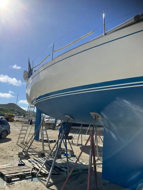 Slide: The Image of A 1979 Nautor Swan 441 is on stands on land. The hull is white with blue stripes. - 7