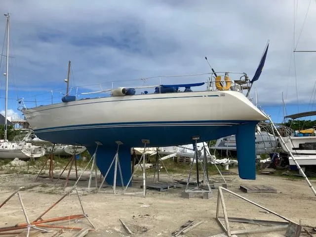 Slide: The Image of A 1979 Nautor Swan 441 is on stands on land. The hull is blue and white. - 10