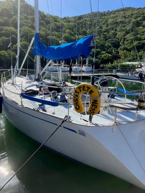 Slide: The Image of A 1979 Nautor Swan 441 is docked in the water, surrounded by green hills. - 4